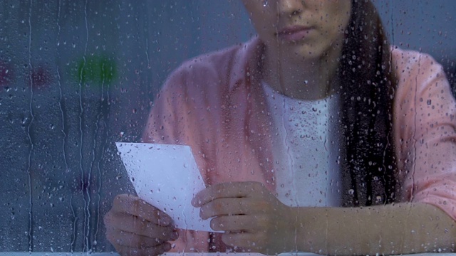 心烦意乱的年轻女子抱着全家福近雨窗，遭受离婚之苦视频素材