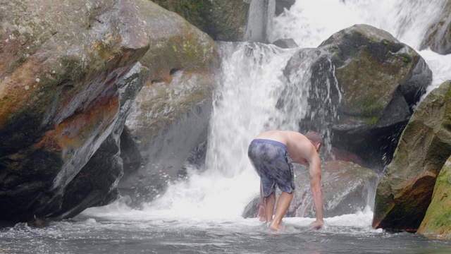 年轻人在激流从热带瀑布在野生丛林。旅行的人站在岩石上从热带雨林瀑布流动的河流。视频素材