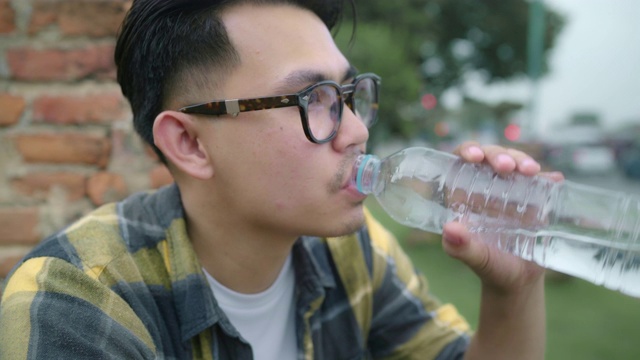 一名亚洲男子在泰国大城府度假后，一边喝水一边放松，男子在传统城市令人惊叹的地标处享受他的旅程。视频素材