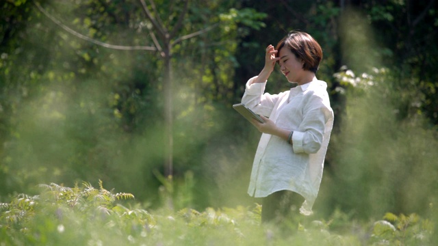 年轻美丽的女人在户外的草地上使用平板电脑视频素材