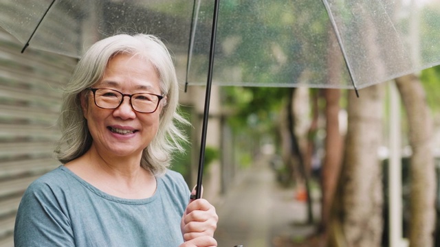 一个快乐的老女人带着伞在一个雨天的城市视频素材