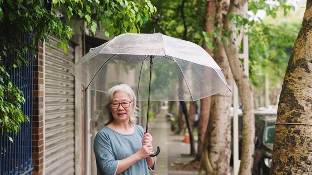 一个快乐的老女人带着伞在一个雨天的城市视频素材