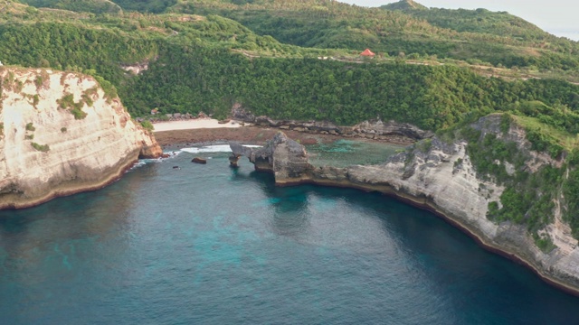 鸟瞰图的绿色热带海岸努沙佩尼达岛，阿图海滩，巴厘岛，印度尼西亚。清澈的蓝色海浪翻滚到海滩。4 k视频素材