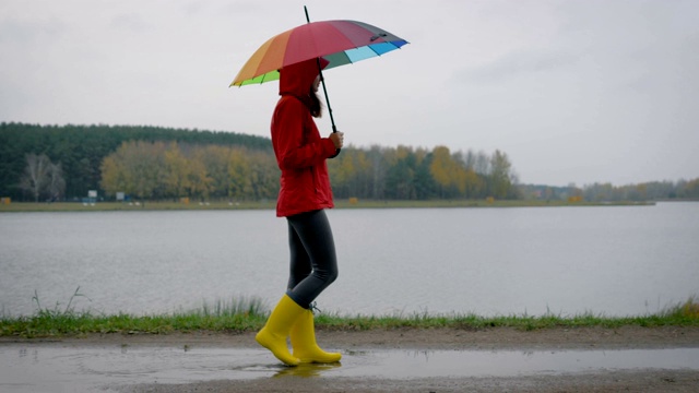 穿着黄色靴子和一把雨伞的女人走过水坑在秋天的一天视频素材