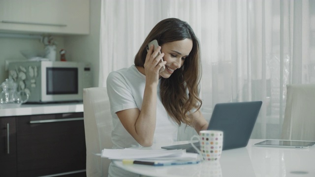 年轻女子在家里厨房打电话。商务女性用手机交谈视频素材