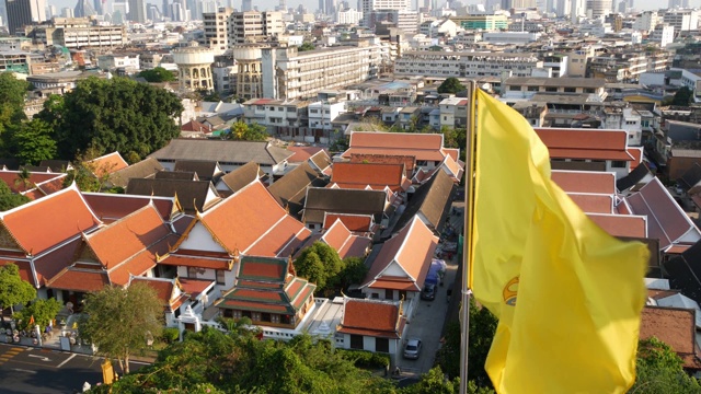 现代东方城镇的城市景观。日落时分，从金山寺可以看到雄伟的曼谷街道上的房屋屋顶。黄色的皇家旗帜和泰国的象征在风中摇曳视频素材