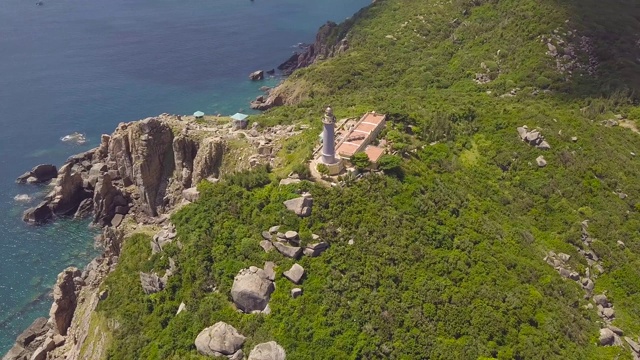 鸟瞰图海上灯塔在绿色的山和岩石海岸。美丽的景观灯塔在悬崖和海岸与蓝色的水无人机视图视频素材