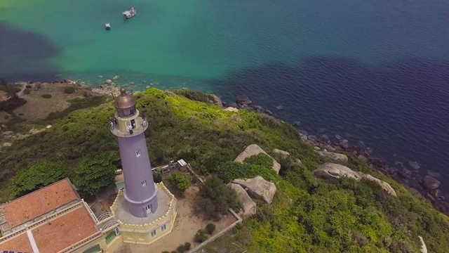 悬崖上的海上灯塔和帆船无人机视图。空中景观海灯塔在绿色的山和船航行在绿松石水视频素材