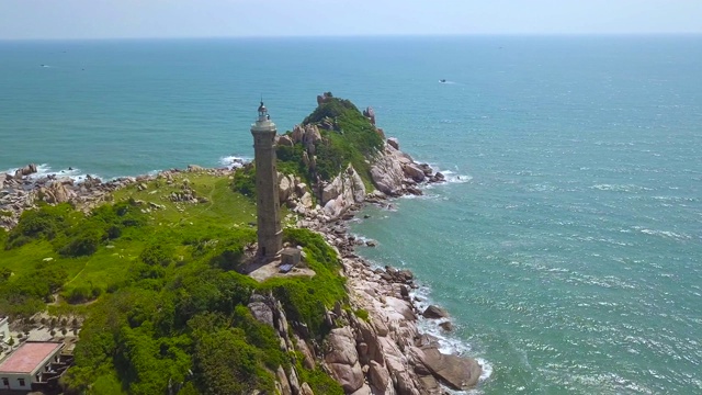 海灯塔在绿色的海岸和蓝色的水空中景观。无人机查看灯塔在海洋和蓝色的水背景岩石岛视频素材