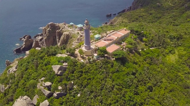 灯塔在绿色的山和岩石海岸蓝色的海鸟瞰图。无人机飞越海上灯塔在高山上的海岸和绿松石水在地平线景观视频素材