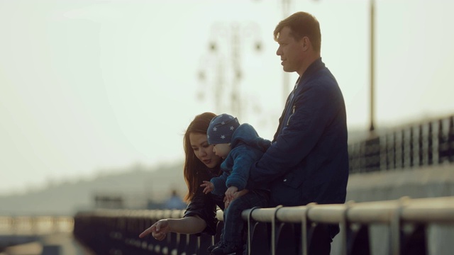 一位东方妇女和她的家人站在栏杆前和她的小儿子说话。妈妈把宝宝带到远处，和他一起玩。快乐的母亲。视频素材