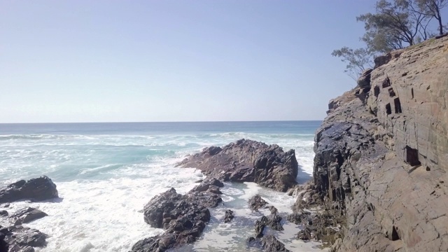 空中向前:岩石洞穴通向岩石覆盖海岸的海洋，努沙，澳大利亚视频素材