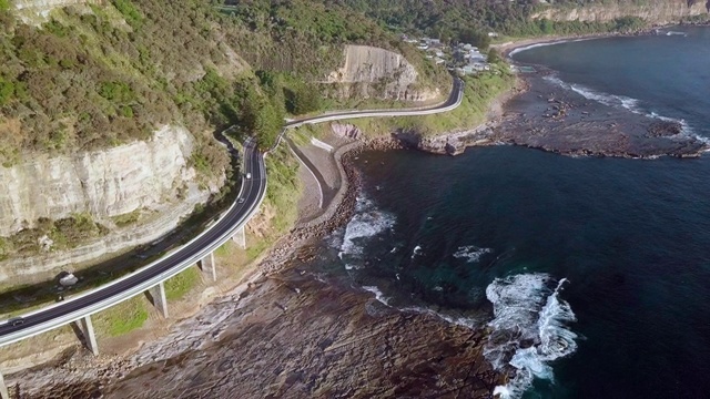 空中盘旋:澳大利亚卧龙岗森林山脉底部，海洋边缘的桥视频素材