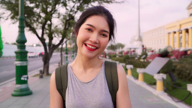 旅行者亚洲女人感觉快乐的微笑相机在曼谷，泰国，背包亚洲女性享受他们的旅程在传统城市惊人的地标。看着相机的人像。视频素材