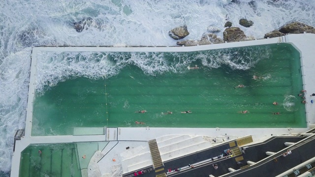 鸟瞰图:巨浪冲入澳大利亚邦迪海滩海边豪华结构的游泳池视频素材