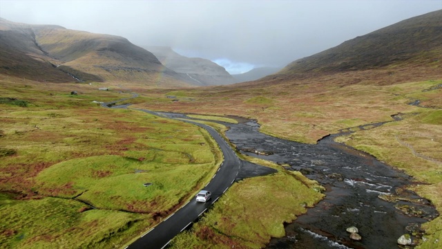 空中汽车沿着蜿蜒的道路行驶，穿过山谷与溪流，斯特雷莫伊岛，法罗群岛视频素材