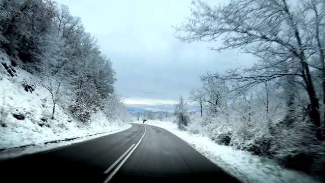 电影中一辆汽车在冬天被雪包围的乡村道路上行驶。挡风玻璃上可见反光和污垢视频素材