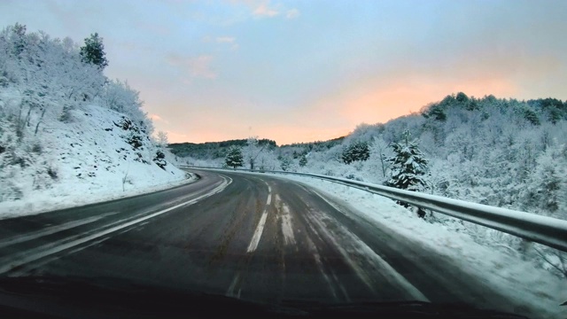 冬天山路上的雪在日出时快速移动。在山区和丘陵附近的乡村道路上驾驶汽车。第一人称视角透过挡风玻璃与反射从内部视频素材