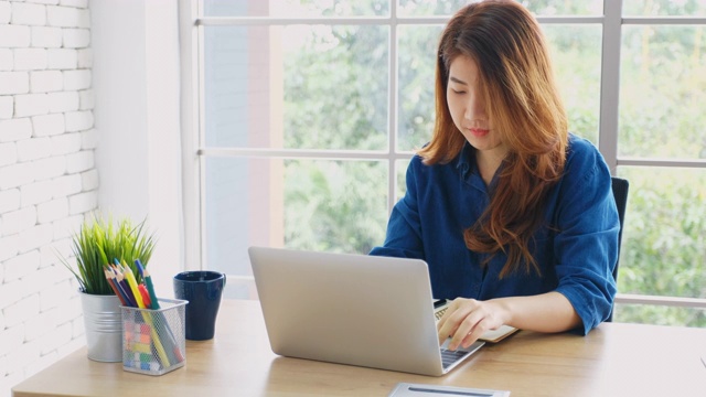 年轻美丽的亚洲女人工作与笔记本电脑，并在家庭办公室注意，人与技术，在家里工作，在线教育视频素材