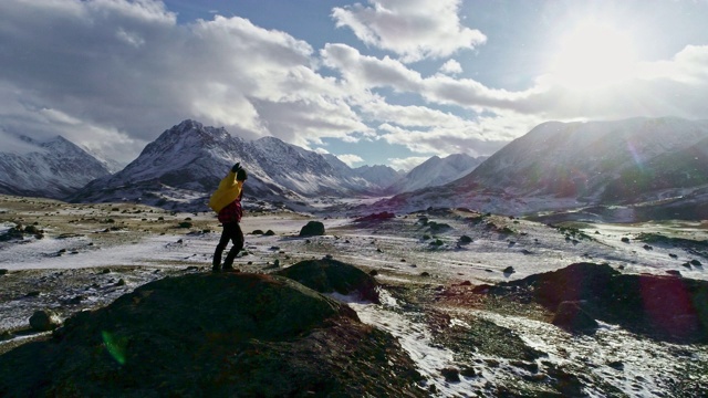 一名男性登山者在雪峰上举起手拿冰锥。登山者在岩石顶端举起双手享受阳光灿烂的日子视频素材