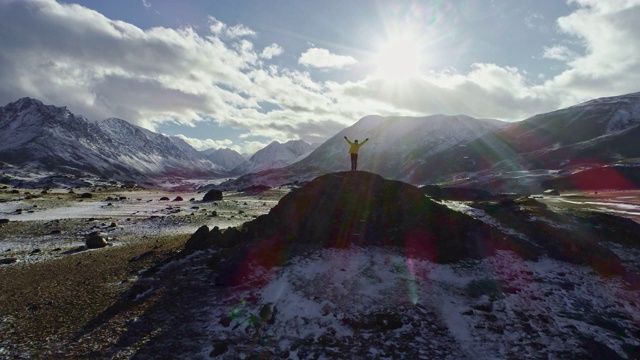 一名男性登山者在雪峰上举起手拿冰锥。登山者在岩石顶端举起双手享受阳光灿烂的日子视频素材