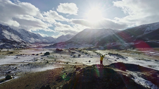 一名男性登山者在雪峰上举起手拿冰锥。登山者在岩石顶端举起双手享受阳光灿烂的日子视频素材