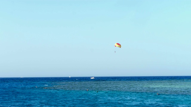 风筝冲浪的降落伞盘旋在水边，映衬着清澈的蓝天。夏天,海景。水面平静，碧海蓝天。度假者戴着面罩在海里浮潜。从海滩到大海的景色视频素材