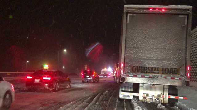 在暴风雪的夜晚，在州际公路上被事故和紧急救援人员拦下时，从一辆车的前面拍摄的视频素材