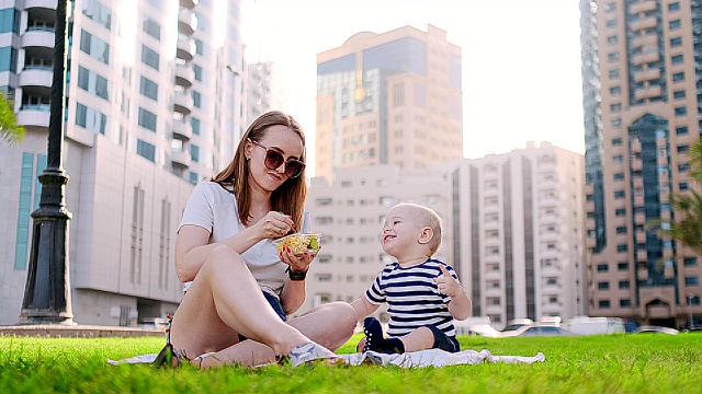 年轻的妈妈带着孩子坐在公园的草地上吃午饭视频素材