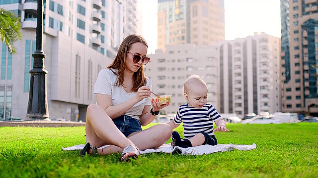 年轻的妈妈带着孩子坐在公园的草地上吃午饭视频素材