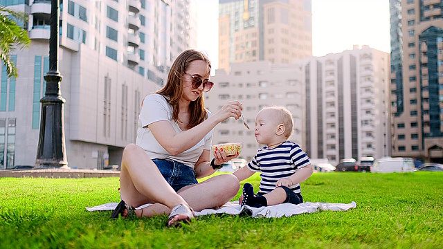 年轻的妈妈带着孩子坐在公园的草地上吃午饭视频素材