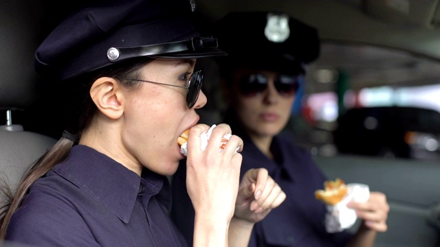 执勤的女警察吃午饭，在警车里吃汉堡，不健康的饮食视频素材