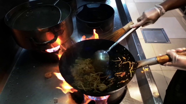 烹饪亚洲食物-在火上用平底锅煮新鲜的面条和蔬菜视频下载