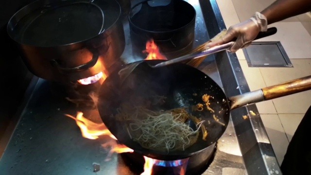 烹饪亚洲食物-在火上用平底锅煮新鲜的面条和蔬菜视频下载