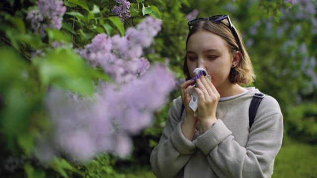 女孩有过敏喷嚏和清洁鼻子在公园附近盛开的鲜花在春天视频素材