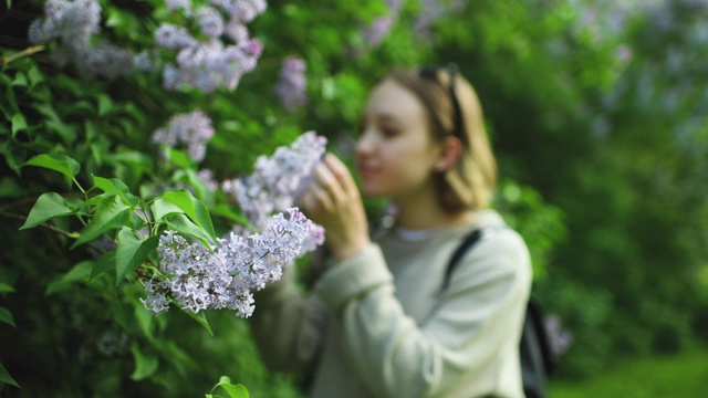 女孩在春天的公园里闻着花香，专注于前景的花朵视频素材