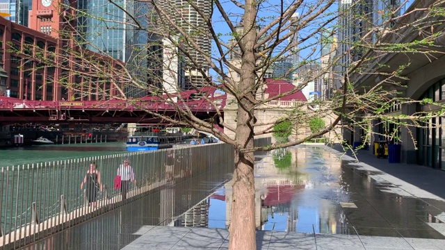 通勤者和游客走在芝加哥河畔的步道上，在那里的喷水池在春天的傍晚创造了城市景观的反射。视频下载