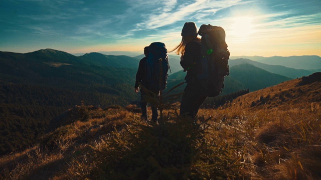 男人和女人在夕阳的背景下走在山上。慢动作视频素材