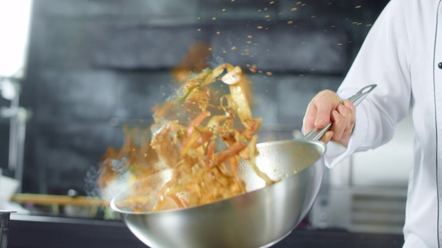 厨师在厨房用火在平底锅里煮食物。厨师亲手准备食物视频素材