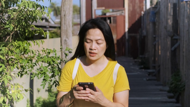 慢镜头亚洲女子关掉手机，走在木桥上，在阳光明媚的日子里游览当地城市视频素材