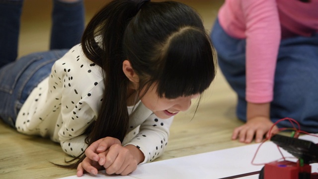 小女孩们近距离观看机器人车在地板上移动视频素材