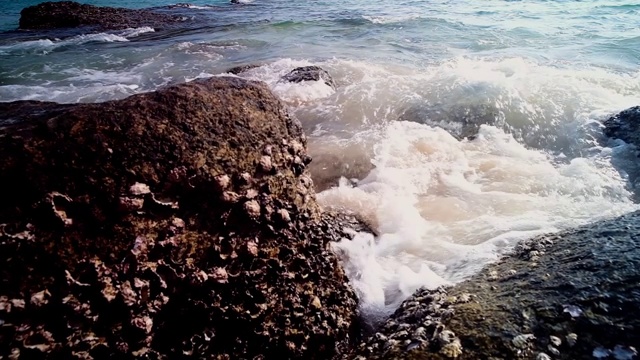 缓慢的运动。泰国普吉岛素林海滩，柔软的海浪拍打着石头，溅起海浪泡沫。视频素材