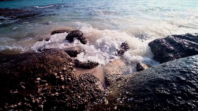 缓慢的运动。泰国普吉岛素林海滩，柔软的海浪拍打着石头，溅起海浪泡沫。视频素材