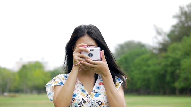 慢镜头美丽年轻的亚洲女人喜欢在公园户外用玩具相机拍照。视频素材