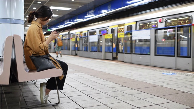 一位年轻女子坐在地铁站的长椅上等待视频下载