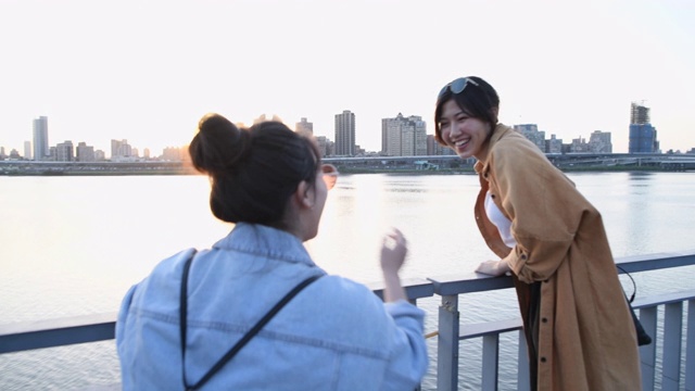 两个年轻的女人在河边欣赏夕阳下的城市风光视频下载