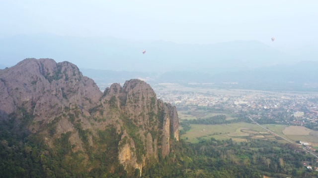 从上面看，一个美丽的石灰岩山在前景和一些热气球在背景令人惊叹的鸟瞰图。万荣、老挝。视频素材