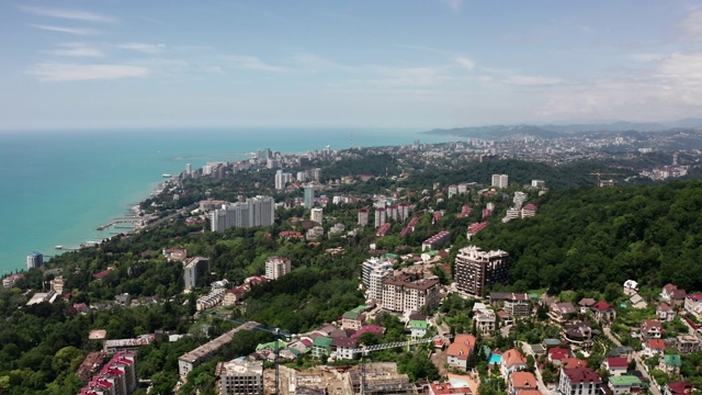 航拍视频拍摄。从索契城的高处俯瞰全景。绿树青山傍海。住宅区域。海滩上的高房子。蔚蓝晴朗的天空。视频素材