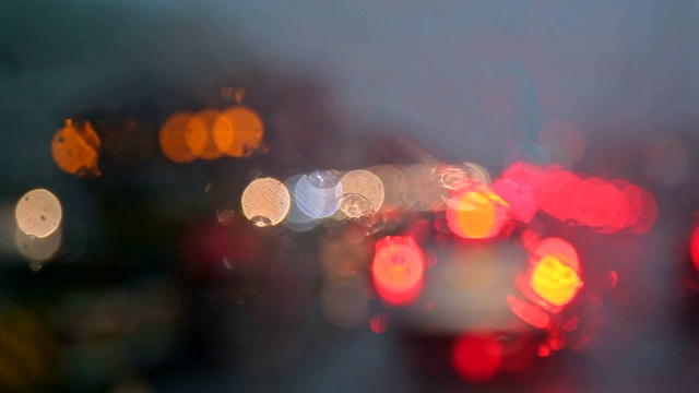 色彩缤纷的散景与路灯在夜晚的雨点落在汽车在道路上的交通，一场暴雨在夜晚。视频素材