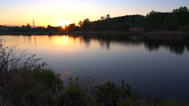 小湖的水在夕阳中缓缓移动，岸边有小房子视频素材